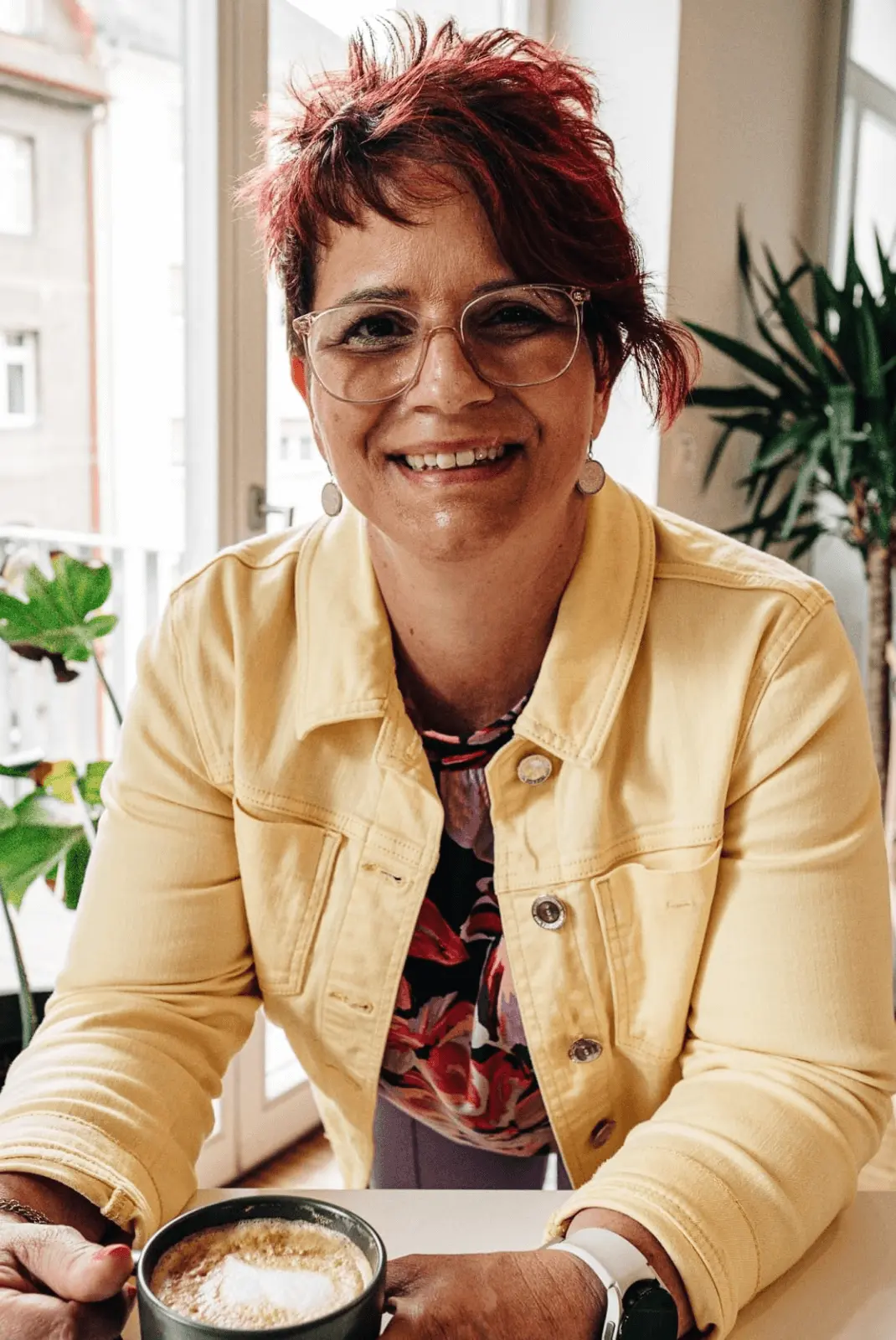 Dozentin Karina P. lächelt im Café mit Kaffee